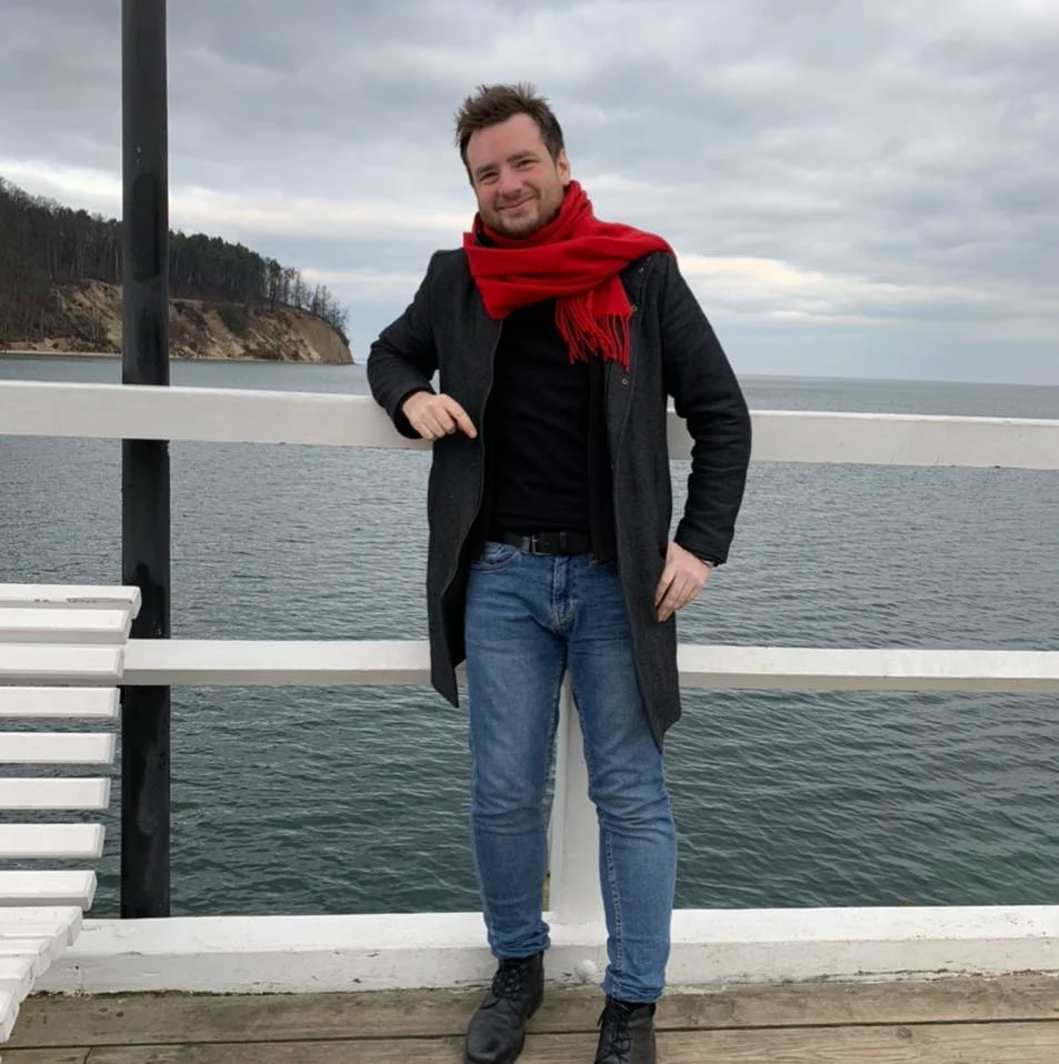 Richard, the creator behind Brit in Poland, standing by the water in a red scarf