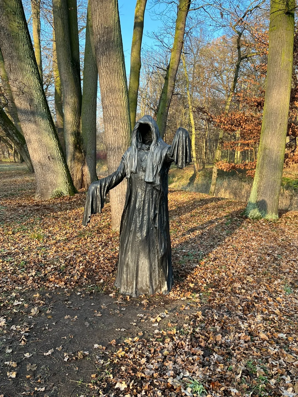 Black hooded sculpture among trees in the park at Uniejów Castle