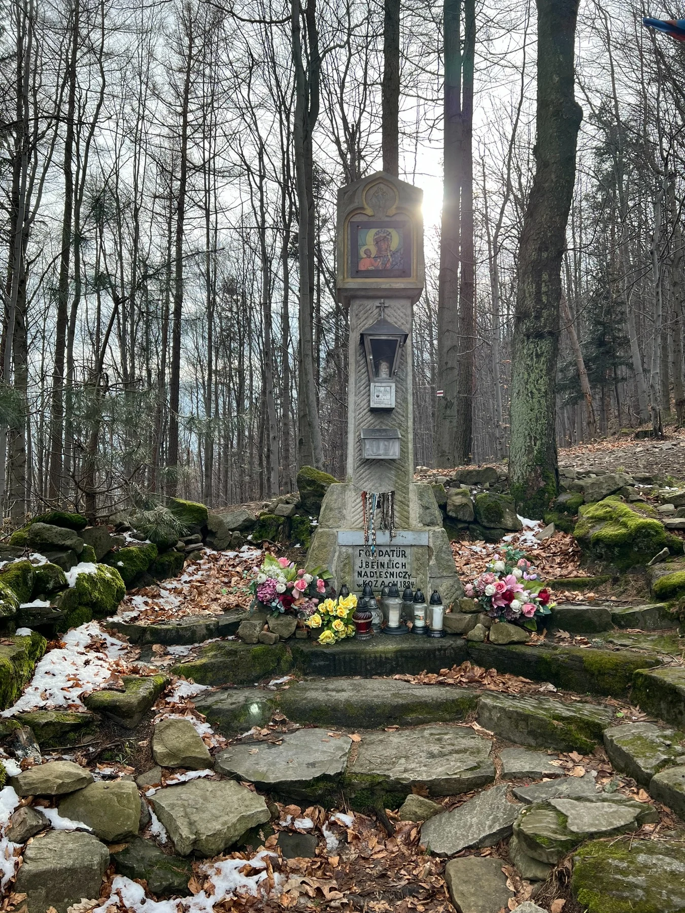 A devotional shrine near Żywiec with candles, flowers and rosaries left by visitors.