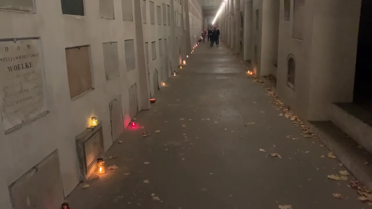 A long, quiet cemetery memorial passage with candles glowing beside wall niches