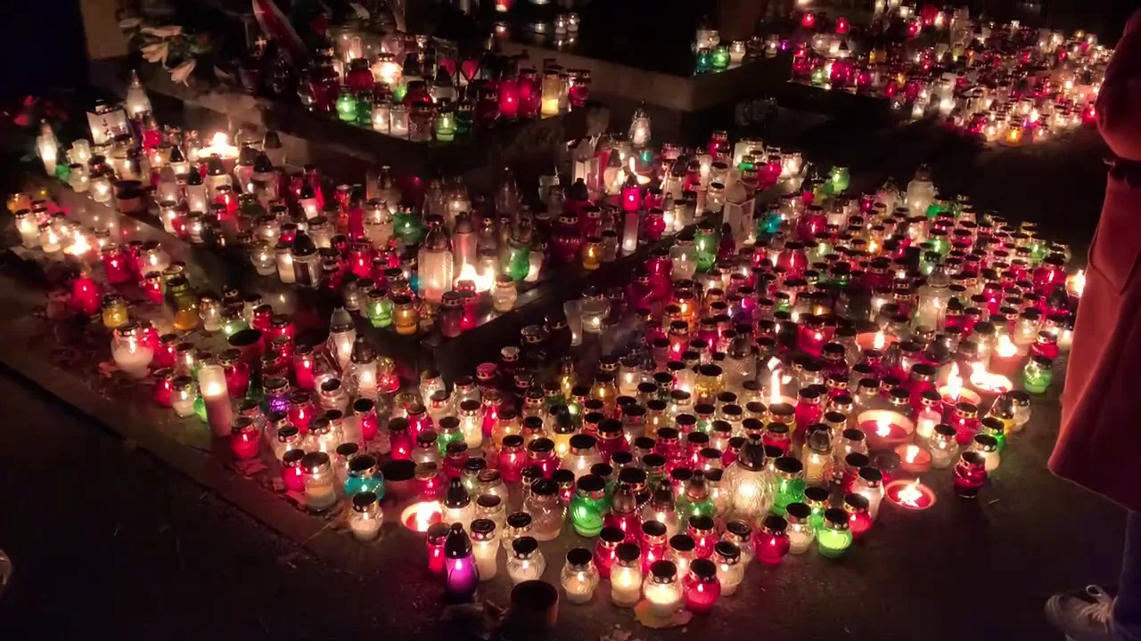 Grave adorned with red and white floral ribbons and candles in Poland