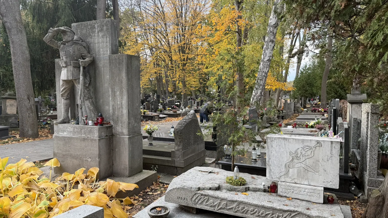 A soldier sculpture and neighbouring graves show the variety of memorial art at Military Powązki.