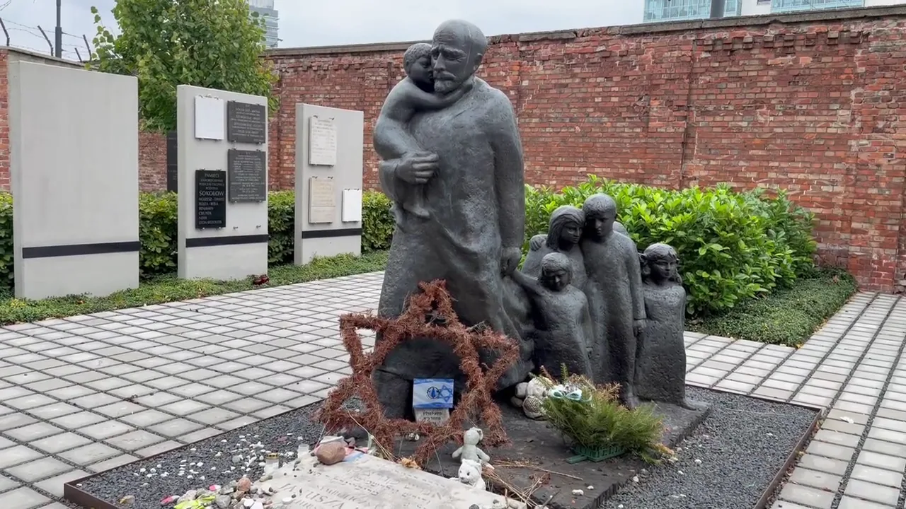Sculpture showing Janusz Korczak with children near a brick wall at Okopowa Cemetery