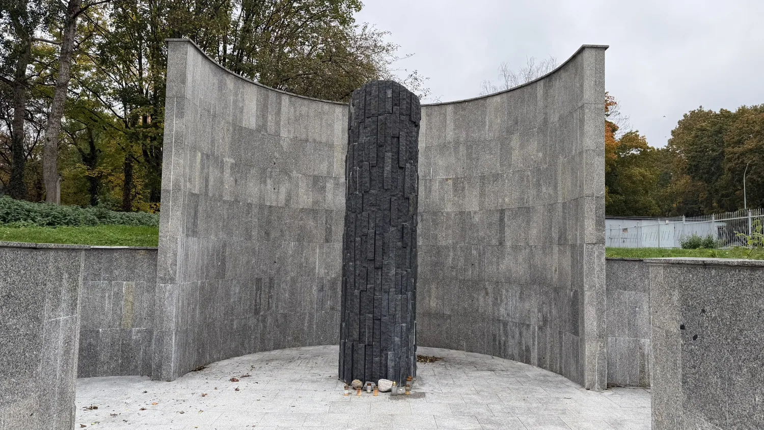 Curving grey stone memorial with a dark central vertical column outside Okopowa Cemetery