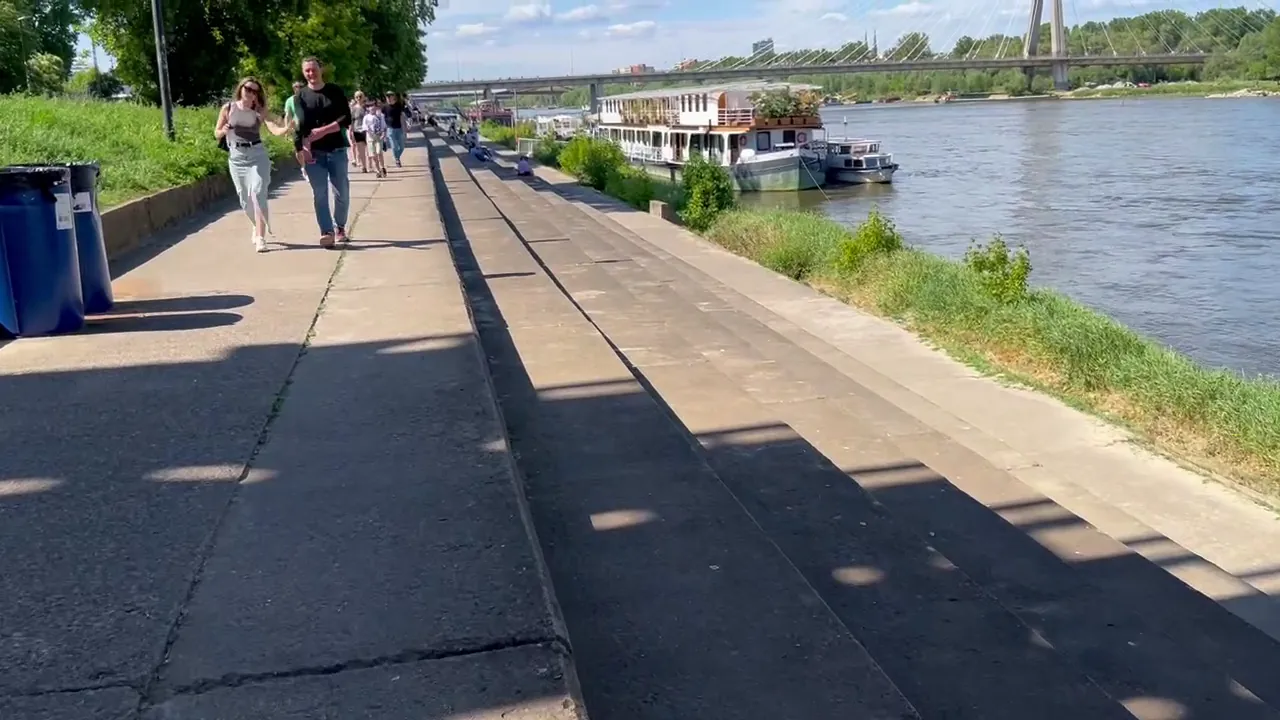 People walking along Warsaw Vistula boulevards beside moored boats